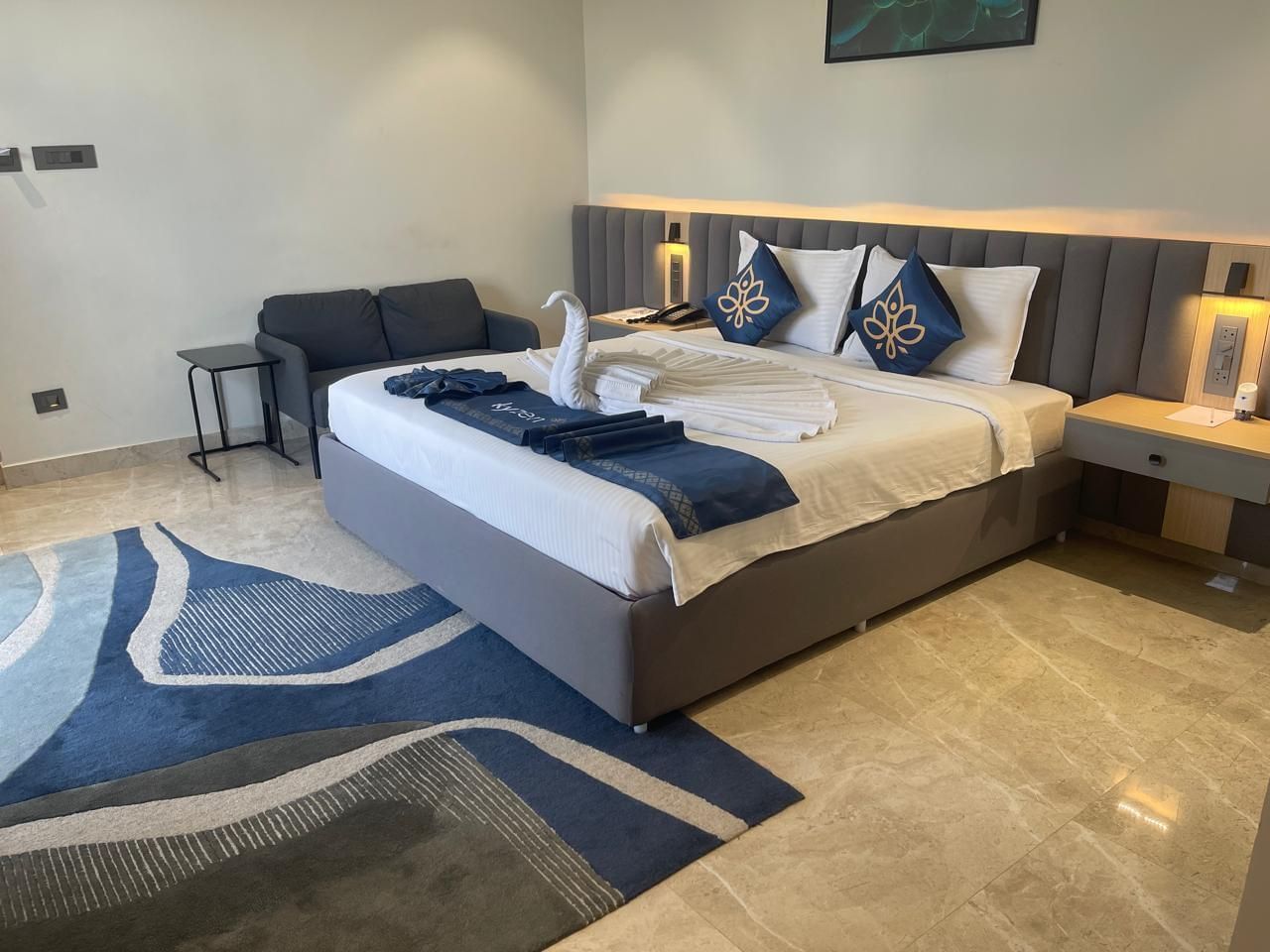 Well lit bedroom at Hotel Kyzen HiTech City with a king bed, blue carpet and a sitting area.